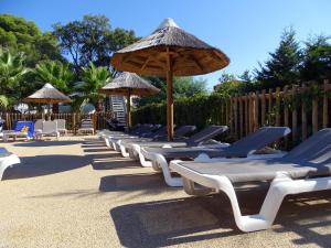 a row of chaise lounges with umbrellas and chairs at Camping de la Treille in Cavalaire-sur-Mer