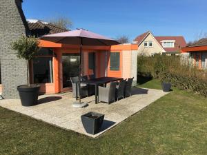 a patio with a table and chairs and an umbrella at Ferienhaus am Meer mit Kamin & Sauna - Seestern 251 in Julianadorp