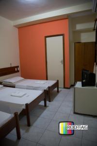 Habitación con 3 camas y pared de color naranja. en Hotel Porto Da Barra en Salvador