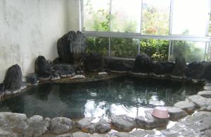 a pool of water with rocks in a room with windows at YOKOSO Ryokan in Beppu