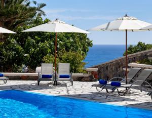 a swimming pool with chairs and umbrellas and the ocean at Terra Blue Santorini in Kamari