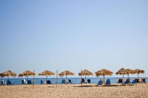 a beach with chairs and straw umbrellas and the ocean at Aselinos Suites in Koukounaries
