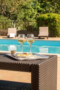 two glasses of wine sitting on a table next to a pool at La Maison Grenadine près du canal du midi in Tourouzelle