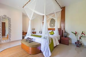 ein Schlafzimmer mit einem Himmelbett, einer Bank und einem Spiegel in der Unterkunft Alosta Luxury Private Villa in Ubud