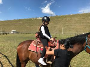 Ein junges Mädchen, das auf einem Pferd reitet, während eine Frau darauf zeigt. in der Unterkunft Green House Oasi Fiume Alento in Prignano Cilento