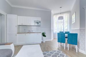 cocina y comedor con armarios blancos y sillas azules en 3 City Apartments - Parkowy, en Sopot