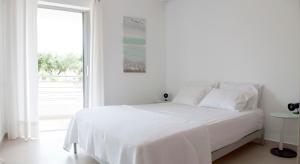 a white bedroom with a bed and a large window at ILIOS H&E house in Elia Laconias