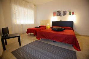 una camera con due letti con lenzuola rosse e una televisione di Dimora Hostel a Agrigento