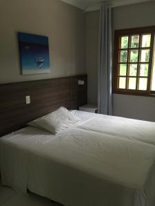 um quarto com uma grande cama branca e uma janela em AP Beira da Lagoa da Conceição em Florianópolis