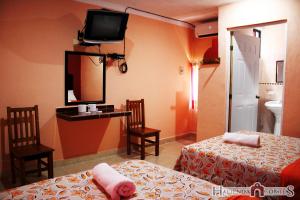 Habitación de hotel con 2 camas y TV en la pared en Hotel Hacienda Cortes en Mérida