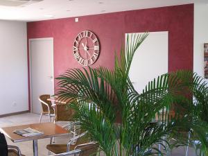 a clock on a red wall with a table and a plant at Hotel le Belvédère in Moustiers-Sainte-Marie