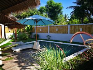a pool with an umbrella and a chair and a table at Villa Saia in Gili Islands