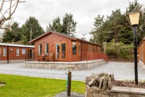 une cabane en bois avec une terrasse couverte dans une allée en gravier dans l'établissement Thistle Lodge, à Auchterarder