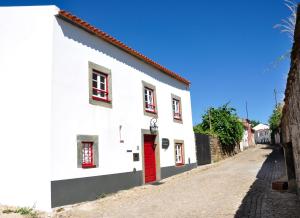 a white building with a red door on a street at Casa dos Hospitalarios in Alvaro