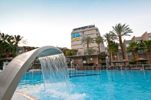 a swimming pool with a water fountain in front of a building at U Coral Beach Club Eilat – Ultra All inclusive in Eilat