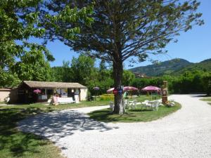 a tree with chairs and umbrellas in front of a house at Camping Notre Dame in Castellane