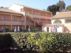 um hotel com guarda-sóis e uma sebe em frente a um edifício em Les jardins de la mer marine de bravone - 2 chambres à lit plus sofa avec piscine à coté mer em Linguizzetta