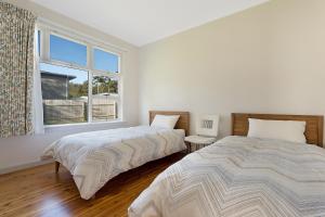 Duas camas num quarto branco com uma janela em The 50's Beach House em Merimbula