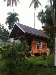 a small wooden house with a porch and palm trees at Eka's Bungalows in Maninjau