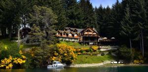 a boat in the water in front of a large house at Dos Bahias Lake Resort in Villa La Angostura