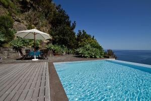 a swimming pool with an umbrella and a table and chairs at Casa de Pedra in Ribeira Quente
