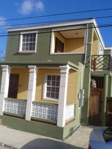 a green and yellow house with a balcony at Believe Caribbean Apartment in Bridgetown