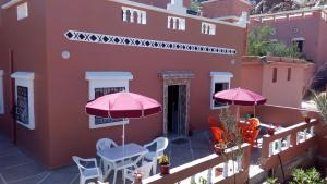 uma varanda com 2 guarda-sóis cor-de-rosa, uma mesa e cadeiras em Maison d'accueil Wakrim em Tafraout