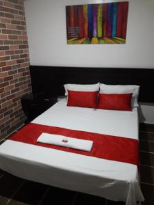 a bedroom with a bed with red pillows and a painting at Hotel Valle de Beraca in Cúcuta