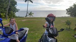 two little girls are sitting on motorcycles by the ocean at Sunset Quay in Rarotonga