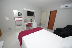 a white bedroom with a bed and a desk and a television at Hotel Leon in Barbalha