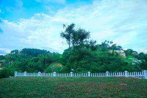 a white fence in front of a hill with a tree at Miyura Holiday Bungalow in Kandy