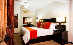 a bedroom with a large bed with red and orange pillows at @The Villa Guest House in Bloemfontein