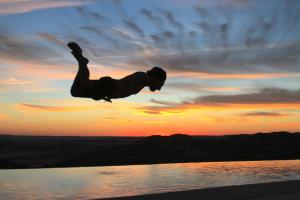 Um homem está a saltar para a água ao pôr-do-sol. em Casas Rurales Planeta Chicote em Zafra de Záncara