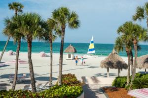 a beach with palm trees and a sailboat on the water at Sandcastle Resort at Lido Beach in Sarasota