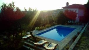 a swimming pool in a yard with chairs and the sun at Villa Mora in Banjol