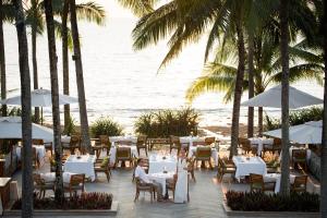 a restaurant on the beach with white tables and palm trees at Trisara - SHA Plus in Nai Thon Beach