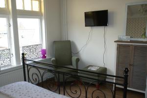 a bedroom with a bed and a chair and a television at Gasterij d'Ouwe Pastorie in Wolphaartsdijk