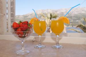 três copos de sumo de laranja e uma taça de morangos. em Guest House Holiday em Korčula