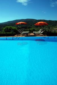 a large swimming pool with two umbrellas and chairs at Residence della Luna in Porto Azzurro
