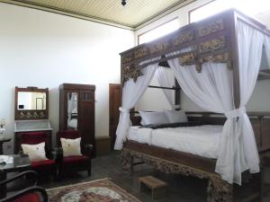 a bedroom with a canopy bed and two chairs at nDalem Natan Royal Heritage in Yogyakarta