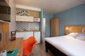 une chambre d'hôtel avec un lit et une chaise orange dans l'établissement Hôtel Baudouin, à Valenciennes