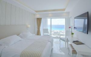 a white bedroom with a bed and a desk and a window at Ibiscus Hotel in Rhodes Town