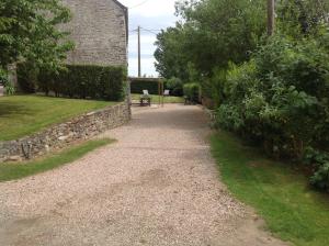 un camino de grava junto a un edificio con un banco en L'Ancien Pressoir en Pierrefitte-en-Cinglais