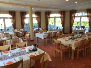 un restaurante con mesas y sillas blancas y ventanas en Landhaus Bergkrone en Willingen