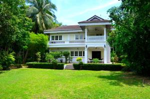 una grande casa bianca con un prato davanti di Baan Khun Nang Colonial Residence a Mae Nam