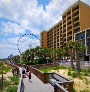 a group of people walking down a boardwalk with a ferris wheel at Holiday Pavilion Resort on the Boardwalk in Myrtle Beach