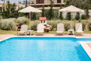 a pool with chairs and umbrellas and a house at Areti Suites in Kathiana