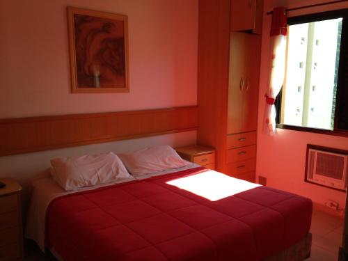 a bedroom with a bed with red walls and a window at Apartamento Guarujá in Guarujá