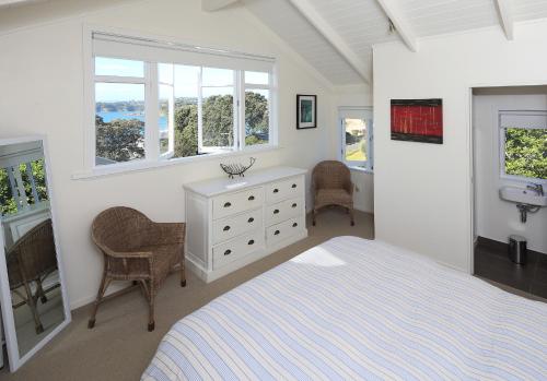 Cape Cottage في Oneroa: غرفة نوم بسرير ومغسلة ونوافذ