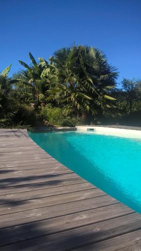 a swimming pool with a wooden boardwalk and palm trees at Cote jardin in Hontanx